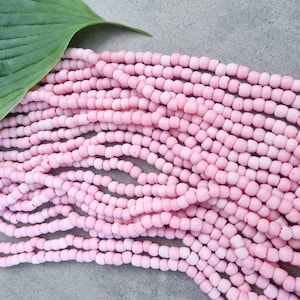 Può includere: Un filo di perle di corallo rosa pallido, ogni perla è piccola e rotonda, le perle sono disposte in un mucchio sciolto su una superficie grigia.