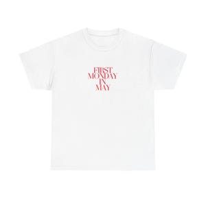 以下が含まれることがあります： 赤い文字で「FIRST MONDAY IN MAY」とプリントされた白いTシャツ