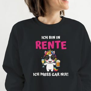 Könnte beinhalten: Schwarzes Sweatshirt mit dem deutschen Text "ICH BIN IN RENTE ICH MUSS GAR NIX!" und einem Cartoon-Einhorn mit Sonnenbrille und Getränk. Das Einhorn hat ein buntes Horn und hält ein Glas und einen Krug.