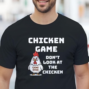 Puede incluir: Camiseta negra con el texto "CHICKEN GAME" sobre un dibujo de un pollo y las palabras "DON'T LOOK AT THE CHICKEN". El dibujo del pollo tiene una cresta roja y las palabras "GAME OVER" en un óvalo blanco.