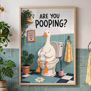 Könnte beinhalten: Ein gerahmter Kunstdruck mit einer weißen Gans, die auf einer Toilette sitzt und eine Rolle Toilettenpapier hält. Der Text lautet ARE YOU POOPING? Der Hintergrund zeigt ein Badezimmer mit türkisfarbenen Fliesen, Schachbrettboden und Pflanze.