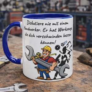 Puede incluir: Taza de cerámica blanca con asa y borde azules, con una caricatura de un trabajador sonriente sosteniendo una llave. La taza tiene texto en alemán que dice: "¡Nunca discutas con un artesano. ¡Tiene herramientas que pueden hacerte desaparecer!"