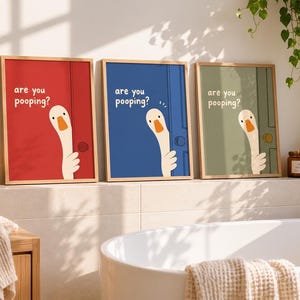 May include: Three framed prints with a humorous design. Each features a cartoon goose peeking from behind a door, with the text "are you pooping?" on red, blue, and green backgrounds. The prints are displayed in a bathroom setting.