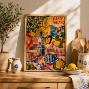 Könnte beinhalten: Ein gerahmter Kunstdruck mit dem Titel CAFFÈ ITALIANO, der eine silberne Mokkakanne, gestreifte Kaffeetassen, eine Schale mit Zitronen und eine Vase mit Oliven auf einer karierten Tischdecke sowie ein italienisches Küstendorf zeigt.