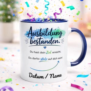 Puede incluir: Taza de cerámica blanca con asa y borde azules, con el texto alemán "Ausbildung bestanden" y otro texto. La taza tiene un diseño de celebración con confeti colorido.