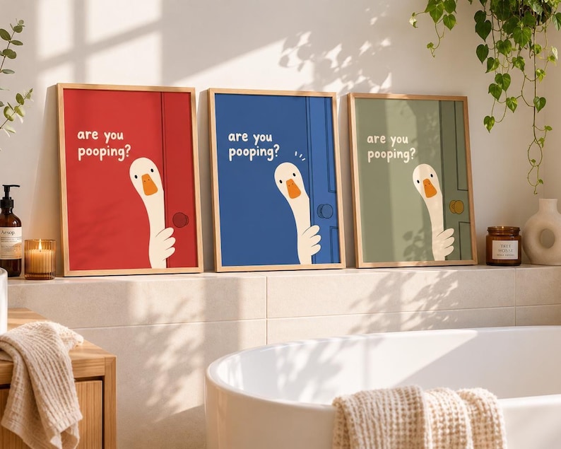Könnte beinhalten: Drei gerahmte Drucke mit einem humorvollen Design. Jeder zeigt eine Cartoon-Gans, die hinter einer Tür hervorschaut, mit dem Text "are you pooping?" auf roten, blauen und grünen Hintergründen. Die Drucke werden in einem Badezimmer gezeigt.