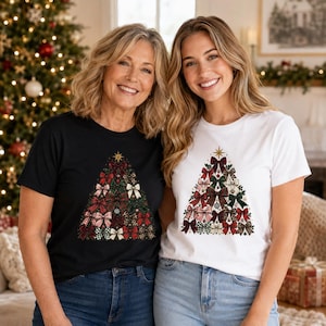 Op de afbeelding: Twee T-shirts met korte mouwen, één zwart en één wit, elk met een grafische print van een driehoekige kerstboom bestaande uit diverse gestreepte strikken in rood, groen en goud, bekroond met een kleine gouden ster.