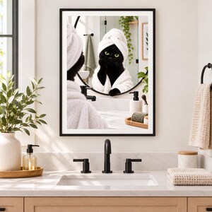 Könnte beinhalten: Ein gerahmter Wandkunstdruck, der eine schwarze Katze mit gelben Augen zeigt, die ein weißes Handtuch auf dem Kopf und einen weißen Bademantel trägt und in einen runden Badezimmerspiegel schaut. Die Spiegelung zeigt die Katze in einem Spa-Ambiente.