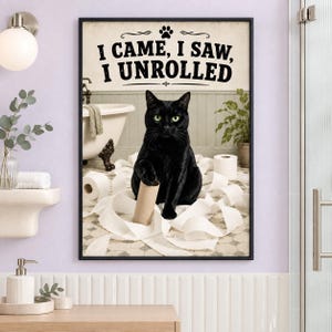 Könnte beinhalten: Ein gerahmter Kunstdruck mit einer schwarzen Katze, die auf einem Badezimmerboden sitzt und von abgerolltem Toilettenpapier umgeben ist. Der Text oben lautet I CAME, I SAW, I UNROLLED. Im Hintergrund sind eine Badewanne und eine Pflanze.