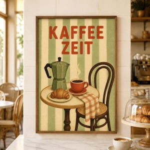 Könnte beinhalten: Ein gerahmtes Wandbild mit dem Text KAFFEE ZEIT in roten Buchstaben über einem runden Tisch mit einer grünen Espressokanne, einer roten Kaffeetasse und einem Croissant auf einem Teller. Ein Holzstuhl mit einem karierten Tuch steht neben dem Tisch.