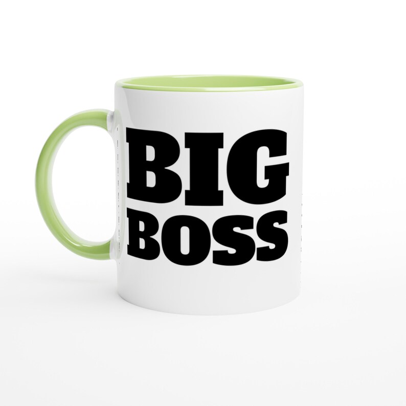 May include: White ceramic mug with a green handle and interior. The mug features the words "BIG BOSS" in bold, black letters. A simple, yet bold design for a coffee or tea cup.
