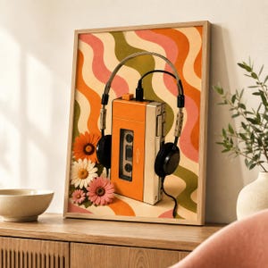 May include: A framed wall art print featuring a vertical orange cassette player with black headphones resting on top. The background displays wavy vertical stripes in orange, pink, and olive green. Three colorful daisy flowers are at the bottom left.