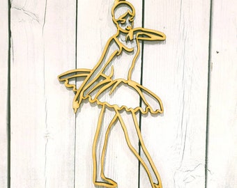 May include: A wooden cutout of a ballerina in a flowing skirt, posed in a graceful dance position. The cutout is painted gold and mounted on a white wooden background.