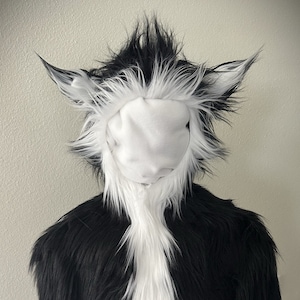 May include: Black and white furry costume head with a white face mask. The costume has long, fluffy ears and a spiky mane.