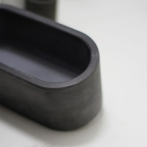 May include: A black oval-shaped concrete planter with a smooth, slightly textured surface.