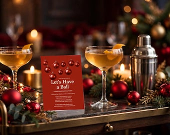 Op de afbeelding: Een rechthoekige rode uitnodigingskaart met de tekst Let's Have a Ball, A Christmas Cocktail Party, voorzien van een afbeelding van rode kerstballen. De kaart staat naast twee cocktailglazen op voet en een metalen shaker.