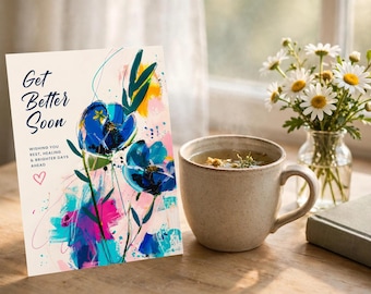 Op de afbeelding: Een wenskaart met de tekst Get Better Soon en Wishing you rest, healing & brighter days ahead, voorzien van een abstract bloemmotief in blauwe, roze en gele verfstreken, naast een keramische mok en een glazen vaas met madeliefjes.
