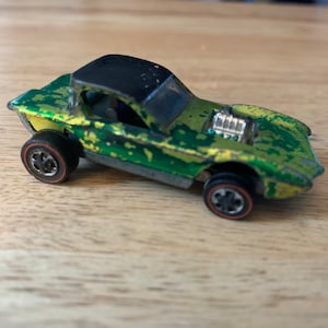 May include: Green and yellow toy car with a black roof and a detailed engine. The car has a worn paint finish and is a vintage Hot Wheels toy.