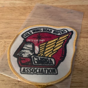May include: A white embroidered patch with a gold border. The patch features a red and gold winged design with a star and the text "Gold Wing Road Riders Association".