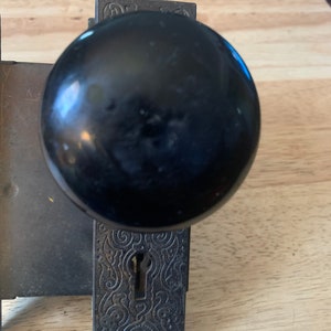 May include: Antique black door knob with a keyhole and ornate design. The knob is made of metal and has a black finish.