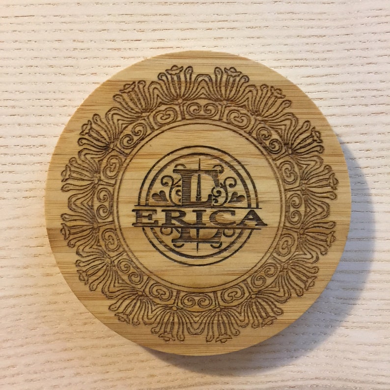 May include: A round wooden coaster with an intricate design and the name "ERICA" engraved in a decorative font.