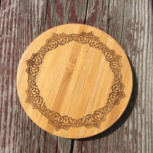 May include: A round wooden coaster with a decorative, intricate design carved into the surface. The coaster is made of light brown wood and has a natural finish.