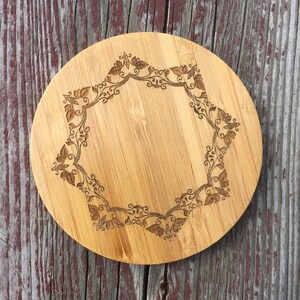 May include: A round wooden cutting board with a decorative floral design carved into the surface. The board is made of light brown bamboo and has a natural finish.
