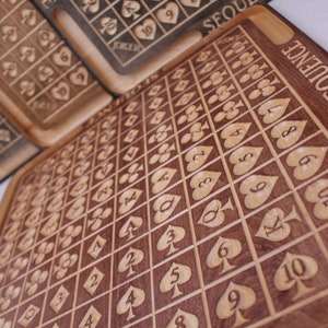 May include: A wooden game board with a grid of squares, each containing a playing card symbol. The board is labeled "SEQUENCE" and has a "JOKER" square.
