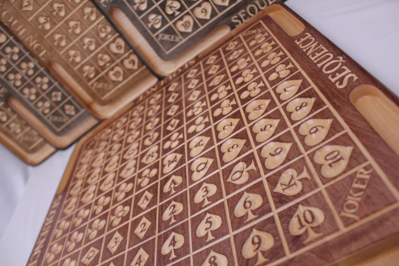 May include: A wooden game board with a grid of squares, each containing a playing card symbol. The board is labeled "SEQUENCE" and has a "JOKER" square.