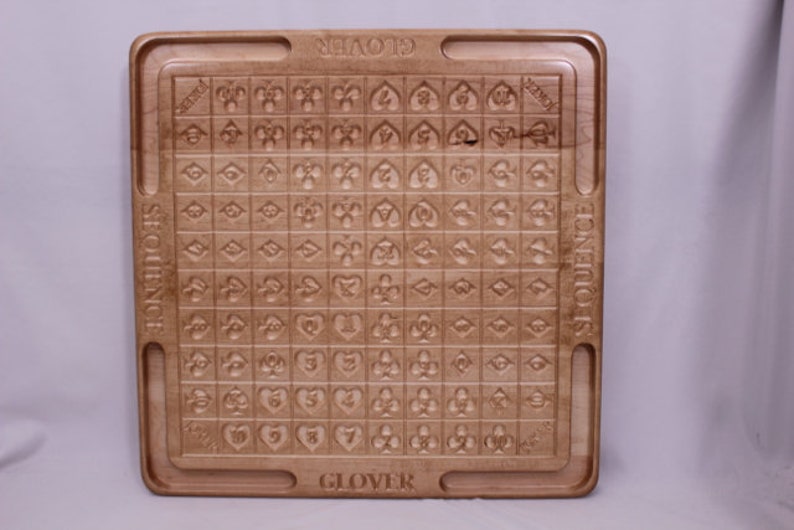 Pu&ograve; includere: Un tabellone da gioco in legno con le parole "SEQUENCE" e "GLOVER" stampate su di esso. Il tabellone &egrave; diviso in una griglia di quadrati, ognuno contenente un simbolo diverso.