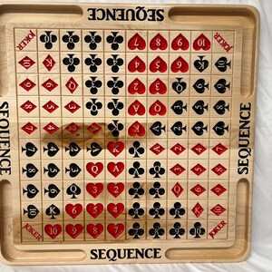 May include: A wooden game board with a grid of 100 squares. Each square has a playing card symbol, including numbers 2 through 10, Jack, Queen, King, and Ace. The board is labeled "SEQUENCE" on all four sides.