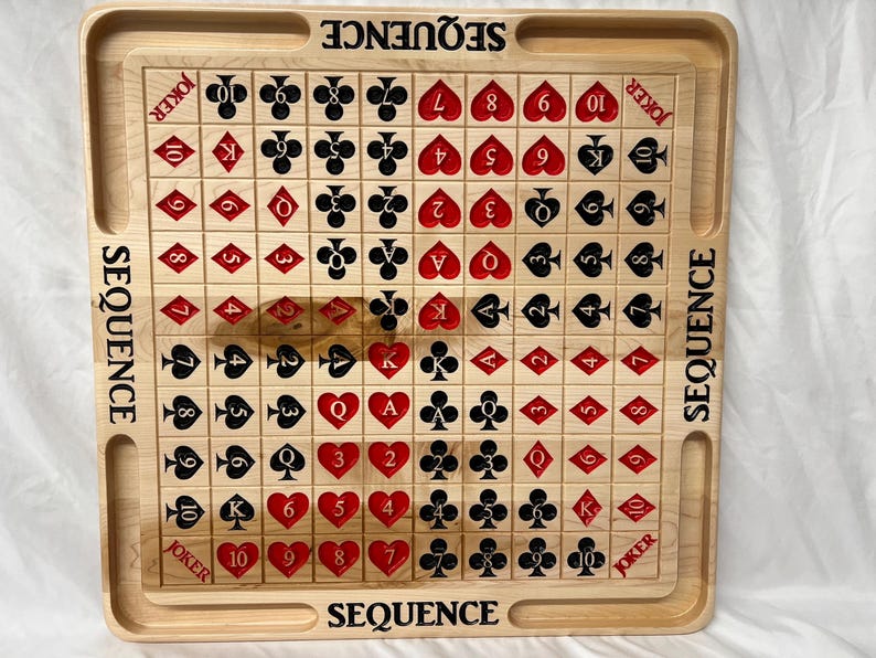 May include: A wooden game board with a grid of 100 squares. Each square has a playing card symbol, including numbers 2 through 10, Jack, Queen, King, and Ace. The board is labeled "SEQUENCE" on all four sides.