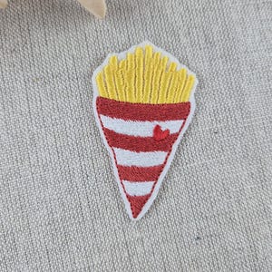 May include: Embroidered patch featuring a cone of golden french fries. The cone is red and white striped with a small red heart. The patch is on a neutral fabric background.