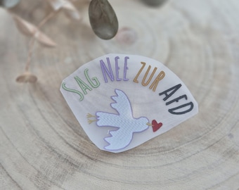 May include: A white sticker with a dove carrying a red heart and the text "Sag Nee zur AfD" in rainbow colors.