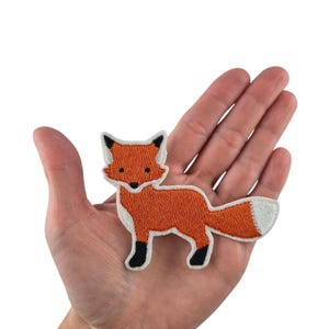 Könnte beinhalten: Orangefarbener gestickter Fuchsflicken mit schwarzen Augen und weißen Akzenten auf weißem Hintergrund.