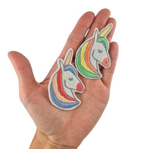 Könnte beinhalten: Drei Keramikbecher mit gesprenkelter, cremefarbener Glasur. Jeder Becher zeigt ein handgemaltes Blumendesign in Blau-, Grün- und Gelbtönen. Die Becher haben eine einfache, abgerundete Form und einen Griff.