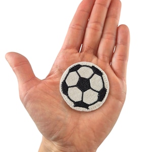 Könnte beinhalten: Ein gestickter Fussball-Patch in Weiß und Schwarz.