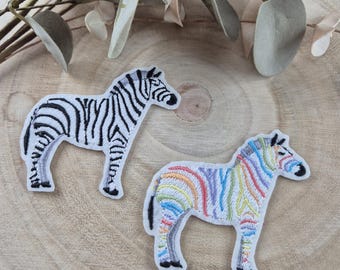 Könnte beinhalten: Zwei gestickte Bügelbilder von Zebras. Ein Zebra ist schwarz-weiß, das andere ein Regenbogenzebra.
