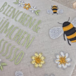 May include: A white card with the text "Bienchen & Imchen sssssso" in green embroidery. The card is decorated with yellow and white flowers and bees.