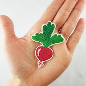 Könnte beinhalten: Ein gestickter Bügelaufkleber mit einem Radieschen mit Blättern in Rot und Grün.