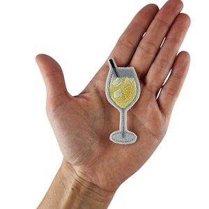Könnte beinhalten: Ein weißer gestickter Bügelaufkleber mit einem Glas Limonade mit einer Zitronenscheibe und Eiswürfeln. Das Glas hat einen Strohhalm, der herausragt.