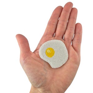 May include: White embroidered iron-on patch of a fried egg with a yellow yolk.
