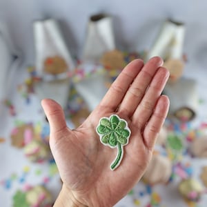 Puede incluir: Un parche bordado de trébol de cuatro hojas verde con un tallo blanco.