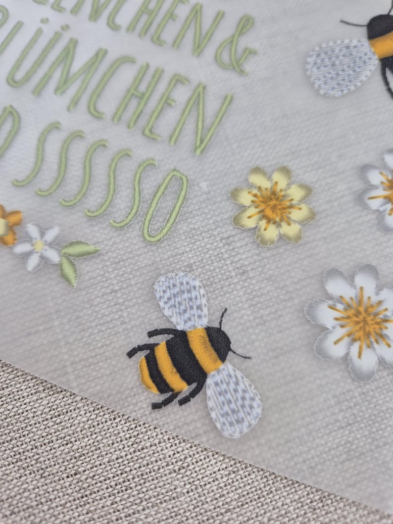 May include: A white background with green text that reads "Bienchen & Bl&uuml;mchen pssssso". There are yellow and white flowers and a black and yellow bee with gray wings.