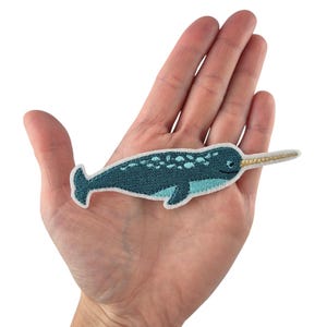 Könnte beinhalten: Ein gestickter Narwal-Patch in Blau und Weiß mit einem goldenen Stoßzahn. Der Patch ist zum Aufbügeln und kann zum Dekorieren von Kleidung, Taschen oder anderen Gegenständen verwendet werden.