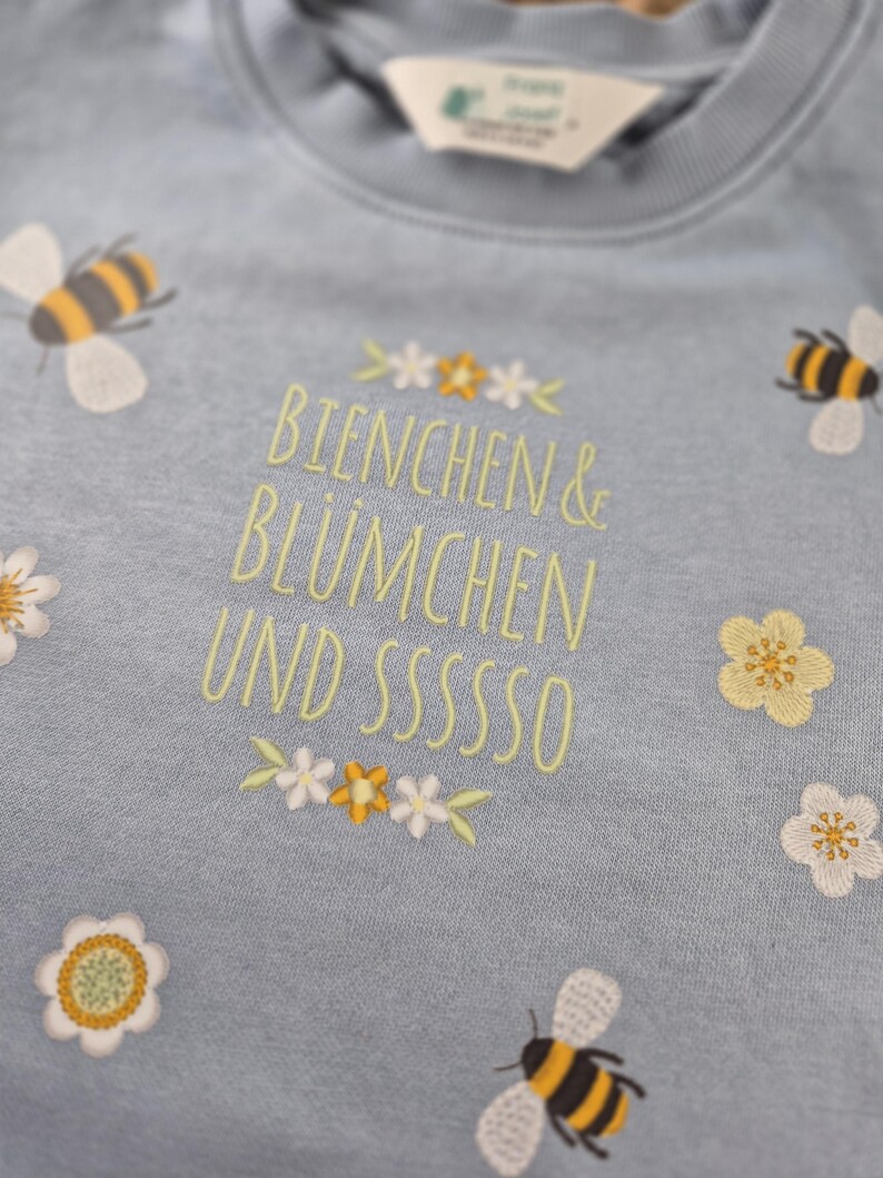 May include: A light blue sweatshirt with embroidered bees, flowers, and the text "Bienchen & Bl&uuml;mchen und sssssso".