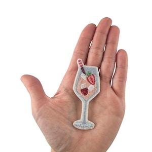 Könnte beinhalten: Ein weißer gestickter Aufnäher mit einem Glas rosa Limonade mit einem rot-weiß gestreiften Strohhalm und Erdbeeren.