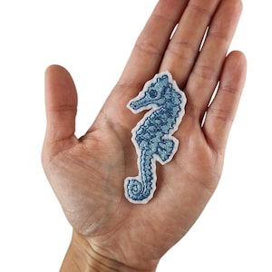 Könnte beinhalten: Ein blauer gestickter Seepferdchen-Aufnäher auf weißem Hintergrund.