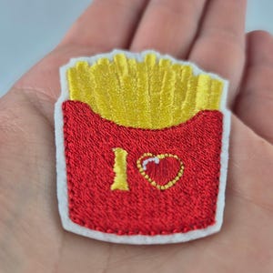 May include: Embroidered patch featuring a red container of golden french fries. The patch has a white border and the words "I ❤️" are embroidered on the container. A fun, food-themed accessory.