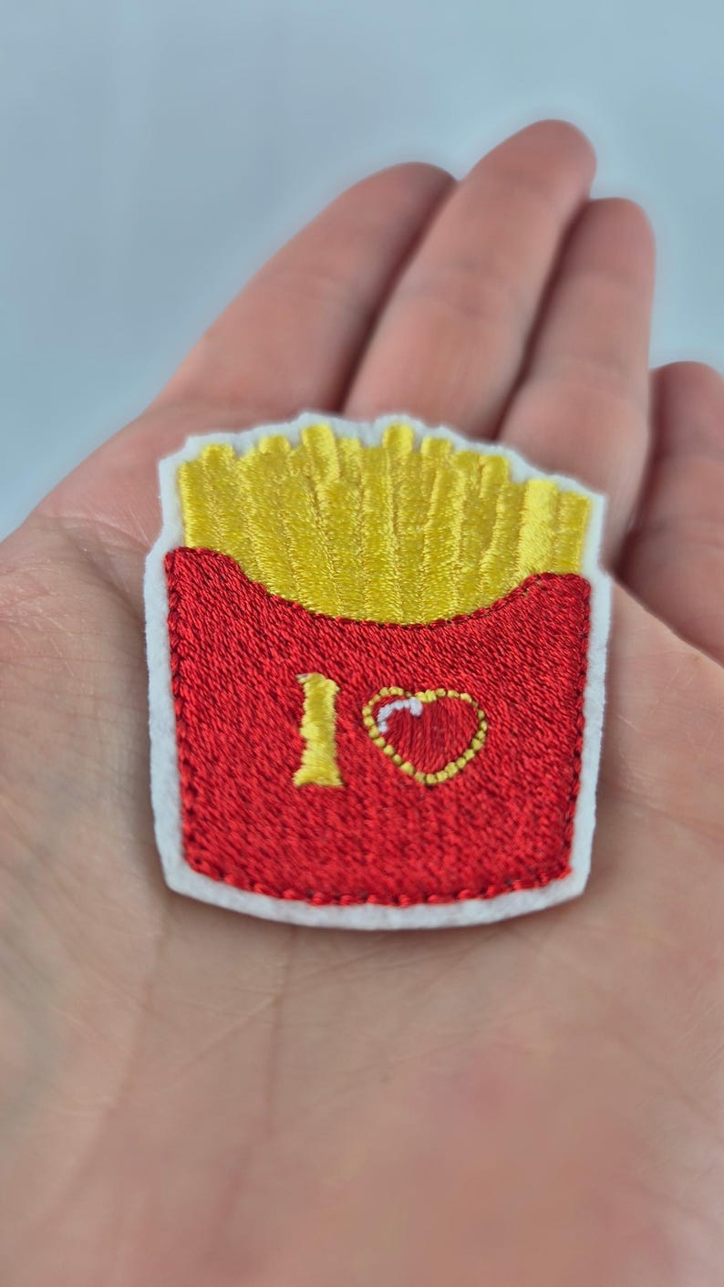 May include: Embroidered patch featuring a red container of golden french fries. The patch has a white border and the words "I ❤️" are embroidered on the container. A fun, food-themed accessory.